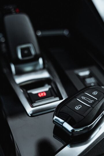 A car key fob rests on a shiny black surface near a modern automatic gear lever—ready for car transport or long-distance removals within the sleek vehicle interior.