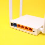 A close-up of the back of a white wireless router with network ports and aerials, set against a yellow background.