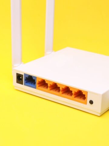 A close-up of the back of a white wireless router with network ports and aerials, set against a yellow background.
