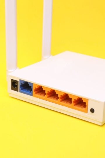 A close-up of the back of a white wireless router with network ports and aerials, set against a yellow background.