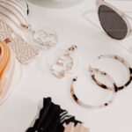 Assorted jewellery and accessories, including hoop earrings, geometric earrings, sunglasses, and stacked fabric hairbands, arranged on a white surface.