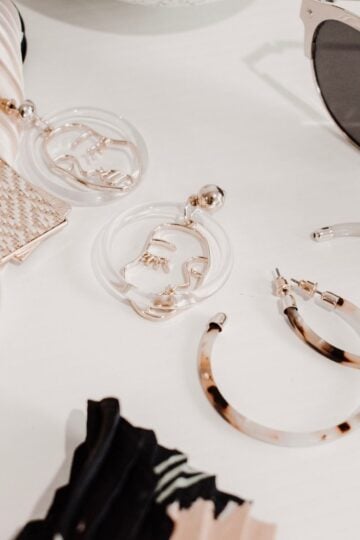 Assorted jewellery and accessories, including hoop earrings, geometric earrings, sunglasses, and stacked fabric hairbands, arranged on a white surface.