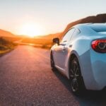 A silver sports car is parked on an empty road during sunset, with mountains in the background and sunlight reflecting off the car-perfect for those considering Hawaii car donation to support local charities.