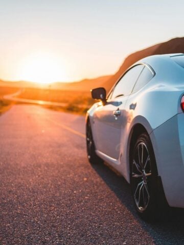 A silver sports car is parked on an empty road during sunset, with mountains in the background and sunlight reflecting off the car-perfect for those considering Hawaii car donation to support local charities.