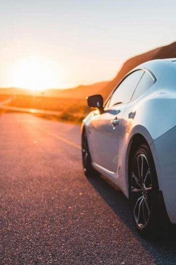 A silver sports car is parked on an empty road during sunset, with mountains in the background and sunlight reflecting off the car—perfect for those considering Hawaii car donation to support local charities.