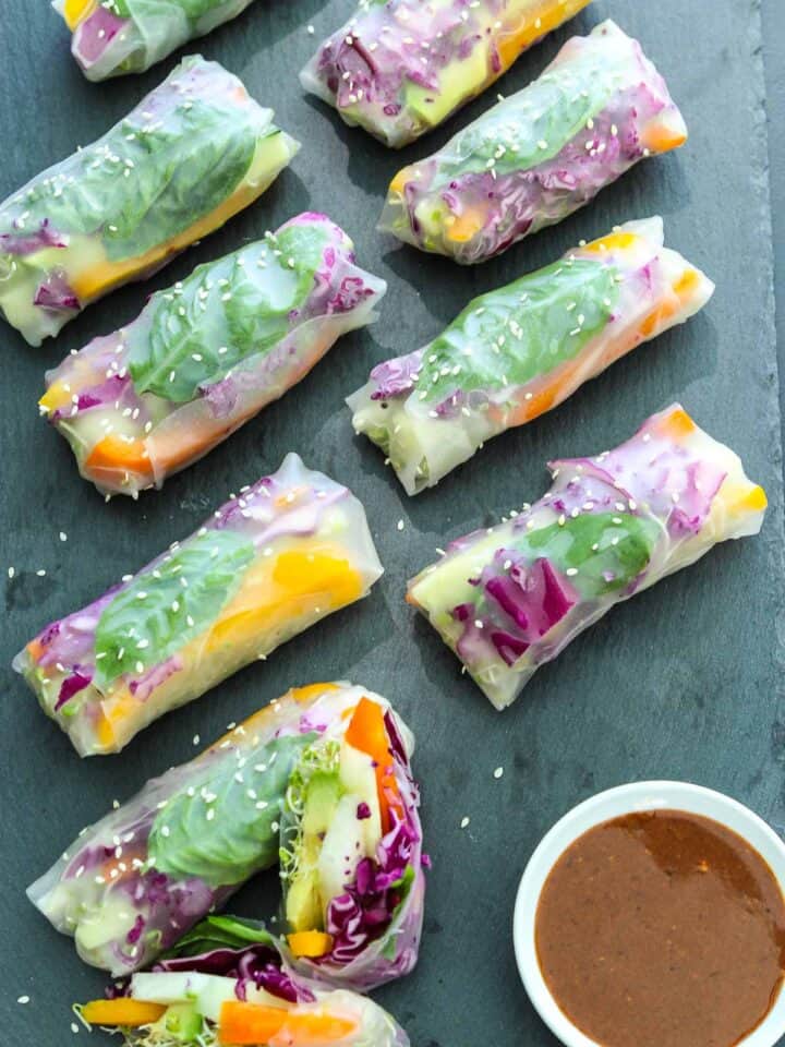 Celebrate With These Recipes for Lunch Ideas on Mother's Day Nine fresh vegetable spring rolls filled with colourful vegetables and leafy greens are arranged on a slate surface, with a small bowl of dipping sauce beside them.