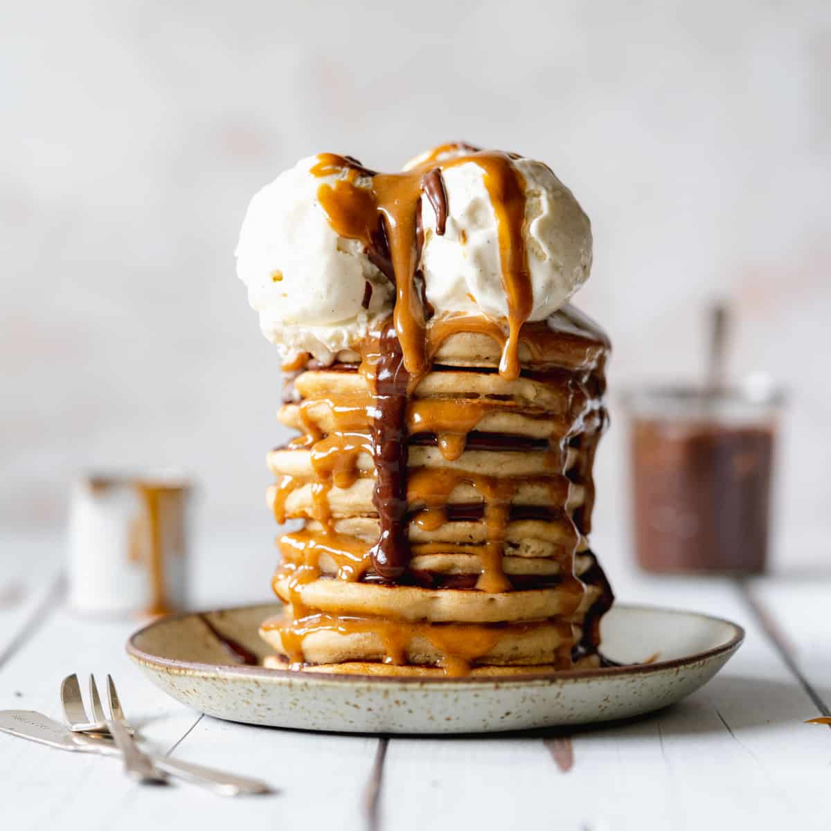 A tall stack of pancakes topped with two scoops of vanilla ice cream and drizzled with chocolate and caramel sauce, served on a plate.