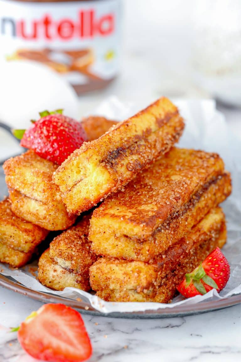 A plate of stacked Nutella-stuffed French toast sticks, coated with cinnamon sugar, garnished with fresh strawberries, with a Nutella jar in the background.