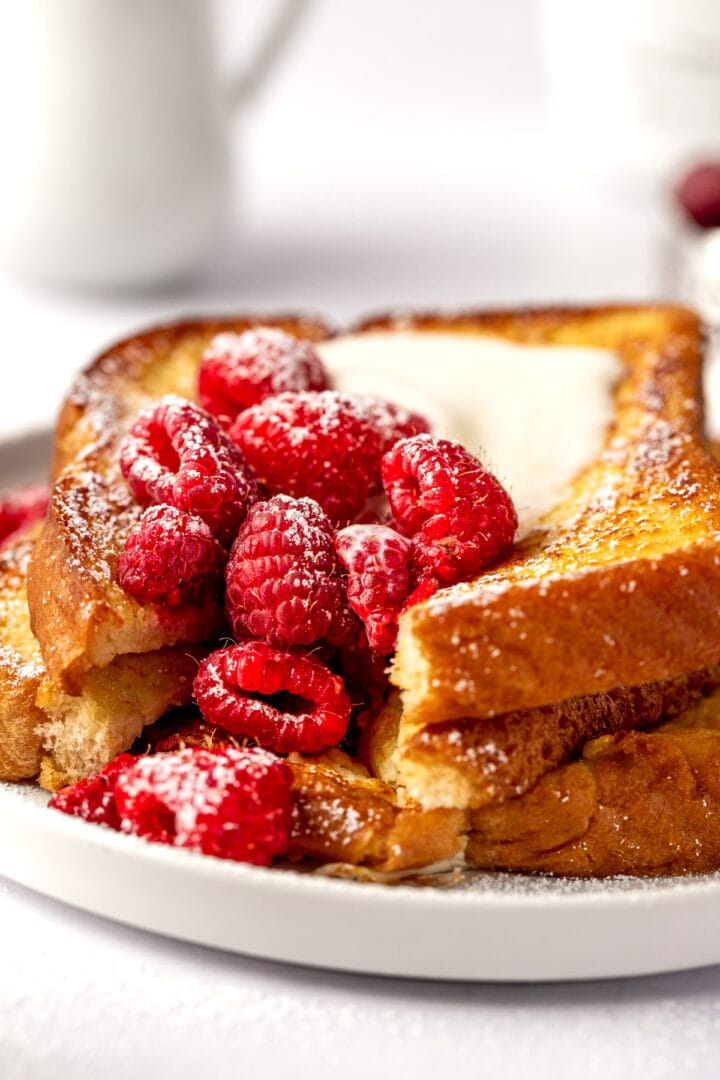 Two slices of eggy bread topped with fresh raspberries and a dollop of cream, served on a white plate.