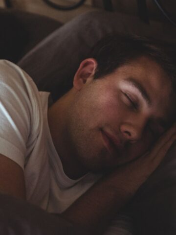 A person wearing a white shirt is lying in bed, sleeping on their side with their head resting on a pillow, enjoying restful sleep.