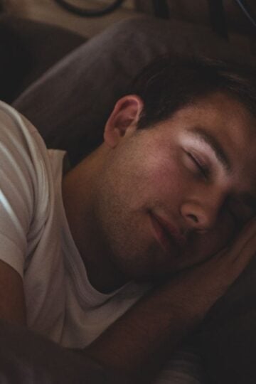 A person wearing a white shirt is lying in bed, sleeping on their side with their head resting on a pillow, enjoying restful sleep.