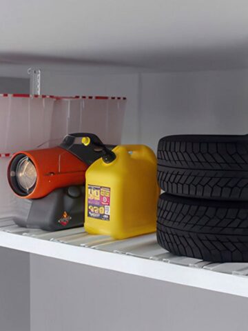 A metal storage shelf holds clear plastic bins, a red and black utility torch, a yellow petrol container, and two stacked car tyres-perfect for those looking to declutter home and keep family clutter under control.