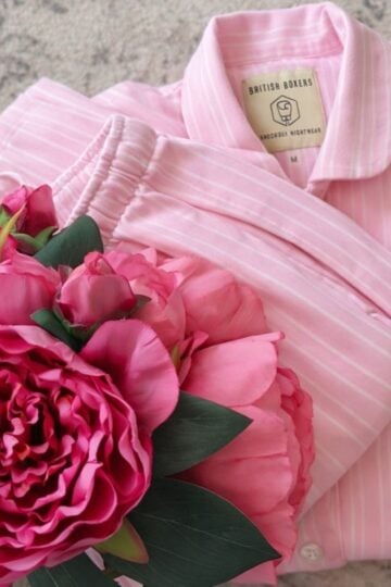 A folded set of Pink Stripe Pyjamas with a British Boxers label, next to a bouquet of pink artificial flowers on a light surface—perfect for your next Pyjamas Review.