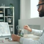 A doctor in a white coat and glasses sits at a desk, offering GP advice to busy families via video call on a laptop, with medicine bottles and office supplies nearby.