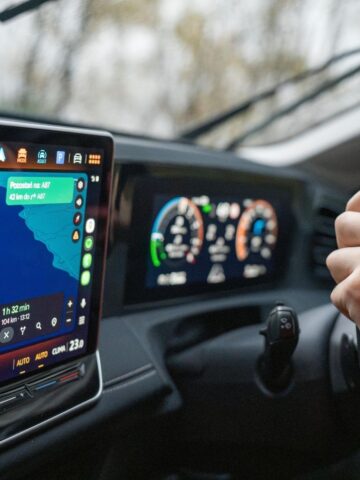 A person drives a car with digital dashboard displays showing navigation, speed, and vehicle information on screens, making road journeys easier and safer with the help of advanced sat nav tracking apps.