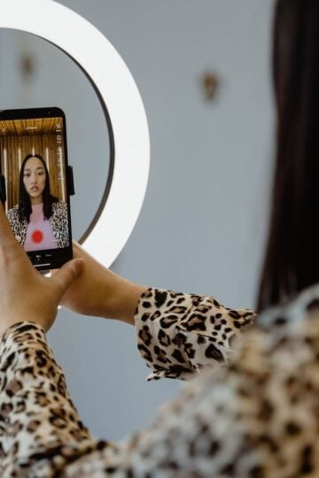 A person in a leopard-print top takes a selfie or films a video with a mobile phone and ring light, capturing the essence of 2026 TikTok growth trends among innovative TikTok creators.