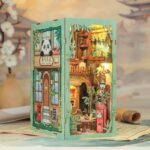 A detailed miniature diorama of a two-storey panda-themed café crafted like wooden book nook kits, featuring bamboo décor, warm lighting, and intricate furniture, with structural panels that align seamlessly against a blurred floral landscape background.