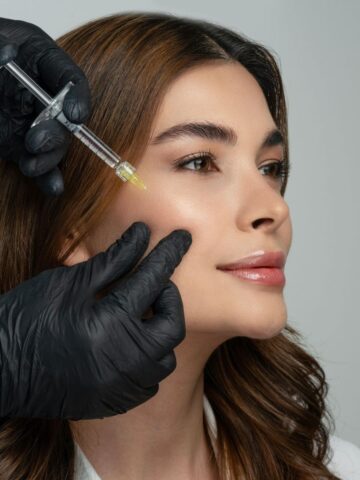 A person receives a facial injection in the cheek from a professional wearing black gloves, showcasing bioremodelling treatments to assess suitability for rejuvenated and youthful skin.