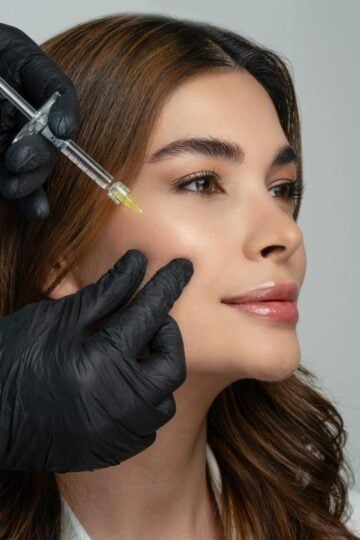A person receives a facial injection in the cheek from a professional wearing black gloves, showcasing bioremodelling treatments to assess suitability for rejuvenated and youthful skin.