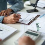 Person analysing financial graphs on documents at a desk with a clipboard, calculator, and papers, carefully checking for audit trail gaps and ensuring a complete audit trail to support an upcoming HMRC review.
