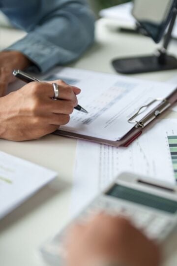 Person analysing financial graphs on documents at a desk with a clipboard, calculator, and papers, carefully checking for audit trail gaps and ensuring a complete audit trail to support an upcoming HMRC review.