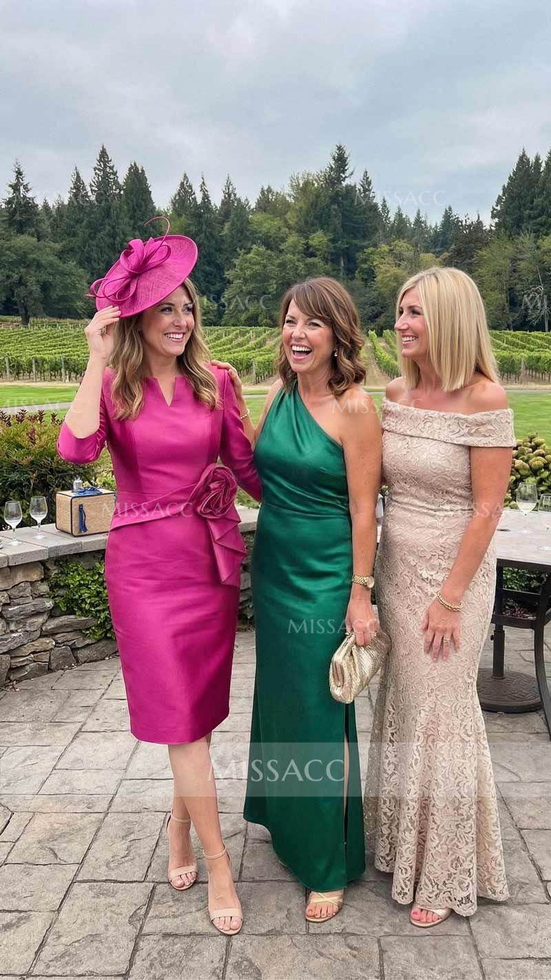 Three women in formal dresses stand outdoors, smiling. One wears a pink dress and hat, the second a green one-shoulder dress, and the third an off-shoulder beige lace dress. Trees and vineyards are in the background.