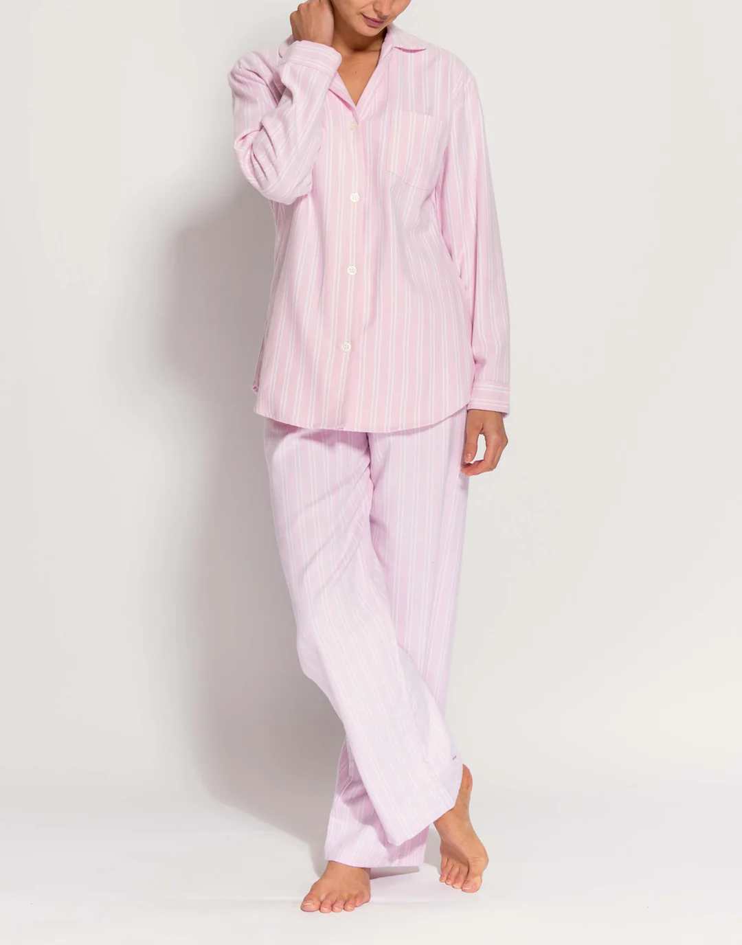 A person wearing British Boxers pink stripe pyjamas with long sleeves and long trousers, standing barefoot against a plain white background.