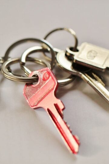 A close-up of a keyring holding several keys, including a prominent red key and a silver replacement filing cabinet key, resting on a light surface.