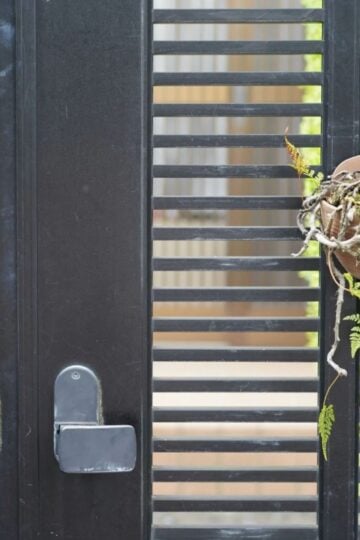 Black aluminium gate with horizontal slats, two silver handles, and a hanging brown pot containing dried plants and some green leaves—combining security with modern style to enhance your property appearance.