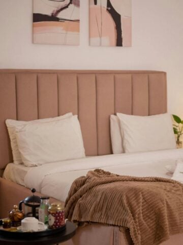 A neatly made bed with white linen, a light brown headboard, beige blanket, and bedside tables with lamps creates a calm bedroom vibe; a tray with tea set completes this inviting family bedroom interior design.