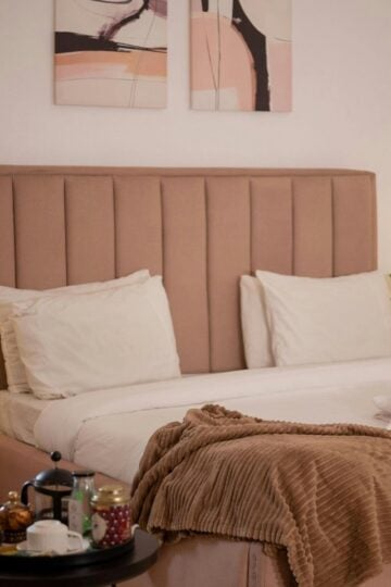 Our Top Interior Design Picks for a Calm Family Bedroom A neatly made bed with white linen, a light brown headboard, beige blanket, and bedside tables with lamps creates a calm bedroom vibe; a tray with tea set completes this inviting family bedroom interior design.