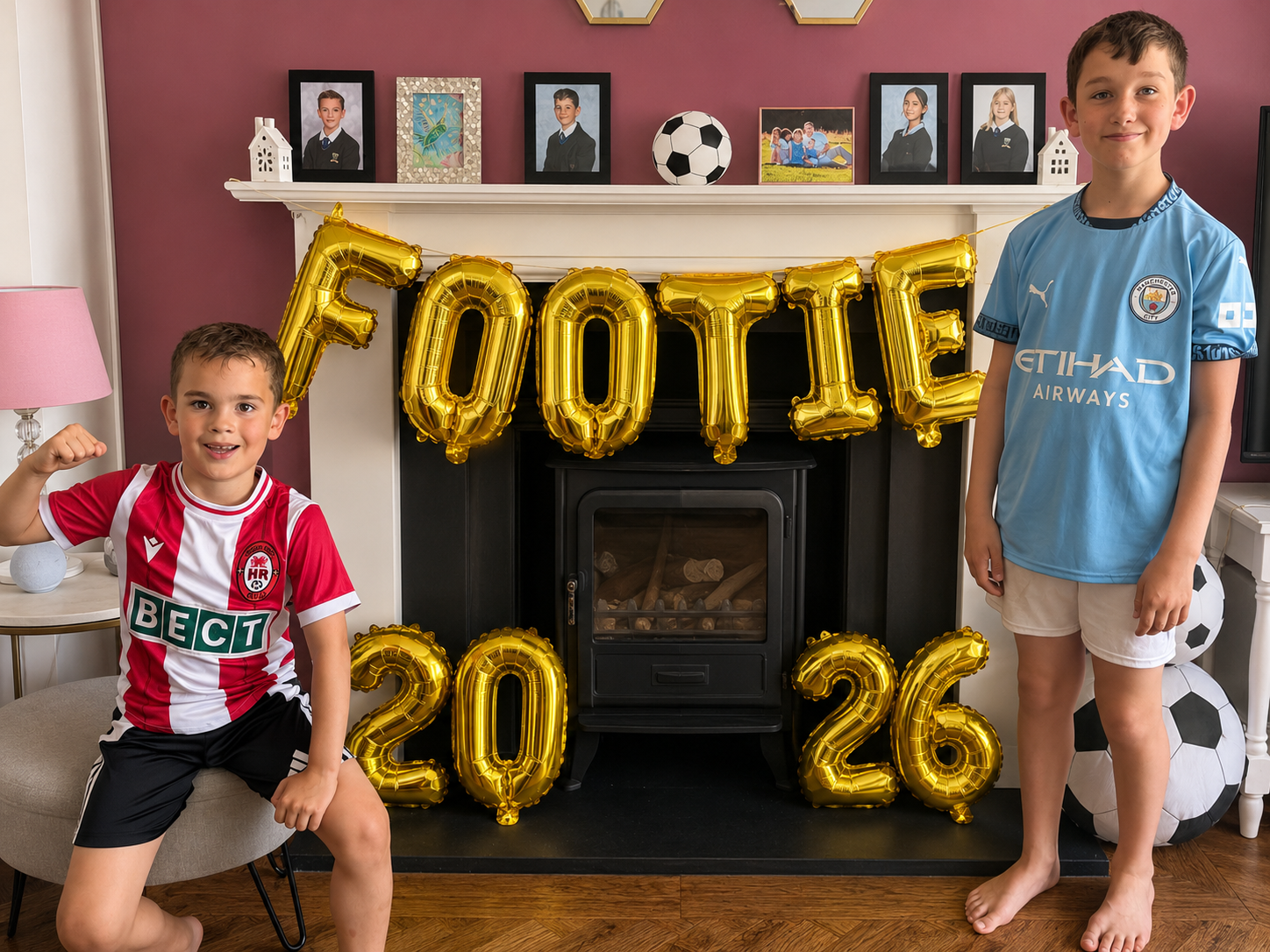 How To Host A Football Watch Party At Home This Summer Two boys in football shirts stand by a fireplace decorated with gold "FOOTIE 2026" balloons and footballs, ready to host at home a summer football watch party, with family photos displayed on the mantelpiece.