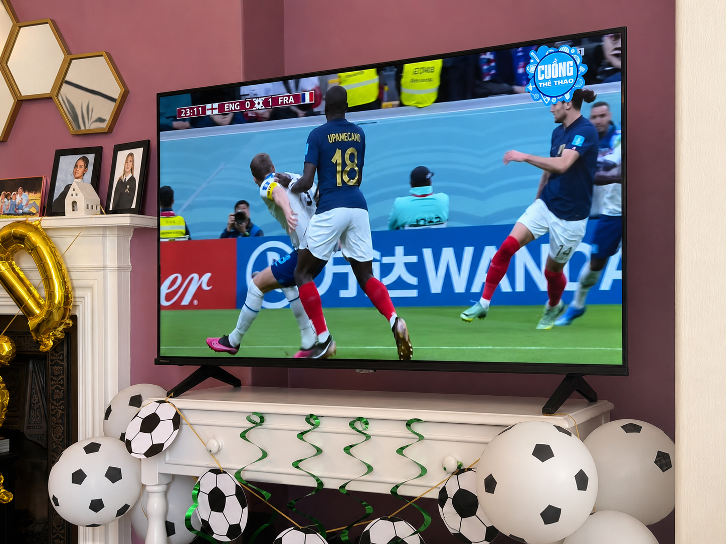 How To Host A Football Watch Party At Home This Summer A television displays a football match between England and France, with players in action; the screen is surrounded by football-themed decorations and balloons for the ultimate football watch party to host at home this summer.