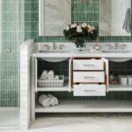 Modern bathroom vanity with open cupboards and drawers, neatly arranged towels, baskets, and a vase of flowers on the worktop-perfect for a family bathroom with stylish green tiles and marble surfaces.