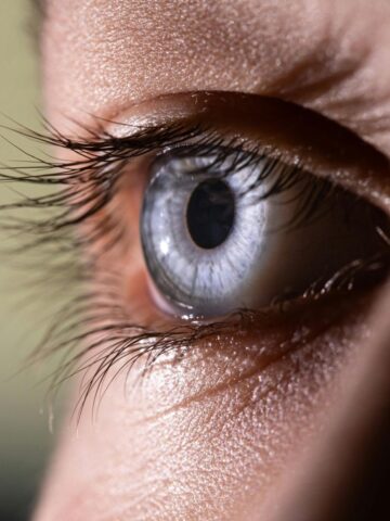Close-up of a human eye with blue iris, showing detailed eyelashes and skin texture.