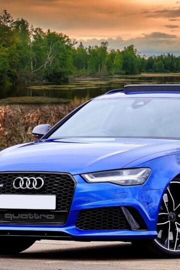 A blue Audi sports car parked outdoors near a lake with trees and a sunset sky in the background, highlighting the importance of regular tyre maintenance for optimal performance, especially when driving an Audi A3 with high-quality tyres.