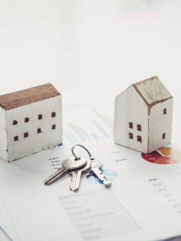 Your First Year in Real Estate: The Tools, Habits, and Mindset That Actually Close Deals Two small wooden house models and a set of keys are placed on printed financial charts and graphs, symbolising essential property tools used to analyse markets and close deals successfully.