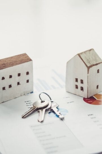 Your First Year in Real Estate: The Tools, Habits, and Mindset That Actually Close Deals Two small wooden house models and a set of keys are placed on printed financial charts and graphs, symbolising essential property tools used to analyse markets and close deals successfully.