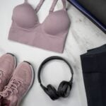 A mauve sports bra, matching mauve trainers, black headphones, and black leggings laid out on a light marble surface-perfect inspiration for buying sports bras that eliminate fit issues.