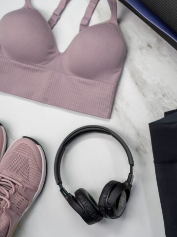 A mauve sports bra, matching mauve trainers, black headphones, and black leggings laid out on a light marble surface-perfect inspiration for buying sports bras that eliminate fit issues.