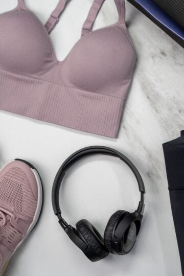 A mauve sports bra, matching mauve trainers, black headphones, and black leggings laid out on a light marble surface—perfect inspiration for buying sports bras that eliminate fit issues.