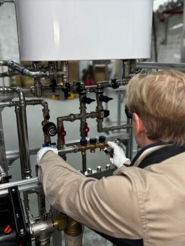 7 Common Mistakes in Industrial Boiler Maintenance A person wearing gloves adjusts valves on a complex system of pipes and gauges in an industrial setting.