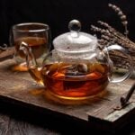 Is Glass the Healthiest Material for Making Tea Every Day? A glass teapot, known for being the healthiest material for making tea, sits on a rustic wooden tray beside a glass cup of tea and dried lavender.