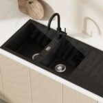 A modern kitchen sink with a matte black tap, two bowls, built-in drainer boards to prevent water pooling, and a wooden chopping board on a white worktop-perfect for clever kitchen tips.