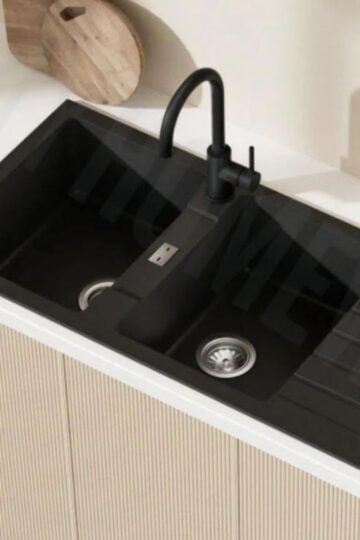 A modern kitchen sink with a matte black tap, two bowls, built-in drainer boards to prevent water pooling, and a wooden chopping board on a white worktop—perfect for clever kitchen tips.