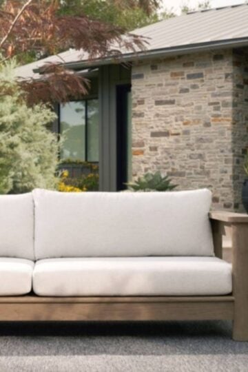 Creating an Outdoor Space That Feels Like Home Outdoor patio with a light-coloured cushioned sofa, a round side table, and plants creates a welcoming outdoor living space in front of a modern stone house.