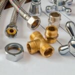 Assorted plumbing fittings and connectors, including a brass T-joint and metal hoses, arranged on top of technical drawings-ideal plumbing parts for DIY renovations.