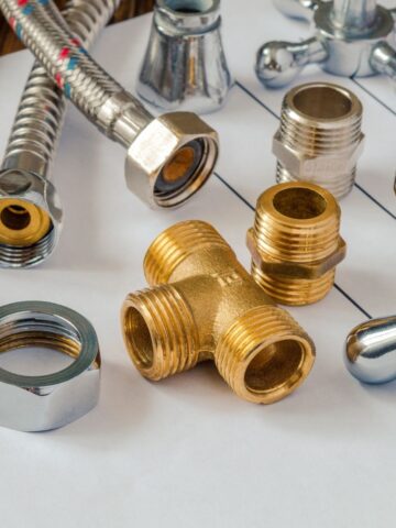 Assorted plumbing fittings and connectors, including a brass T-joint and metal hoses, arranged on top of technical drawings-ideal plumbing parts for DIY renovations.