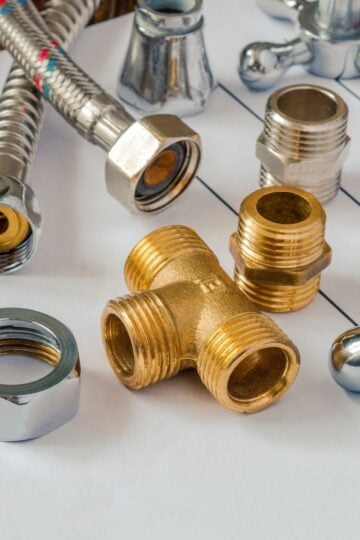 Small Plumbing Parts That Make a Big Difference in DIY Renovations Assorted plumbing fittings and connectors, including a brass T-joint and metal hoses, arranged on top of technical drawings—ideal plumbing parts for DIY renovations.