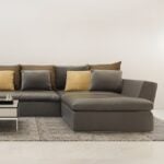 How Modular Lounges Create Space-Saving Living Solutions A modern sectional sofa with grey upholstery and space-saving design, paired with brown and yellow cushions, sits on a textured rug beside a black and white coffee table against a plain white wall.
